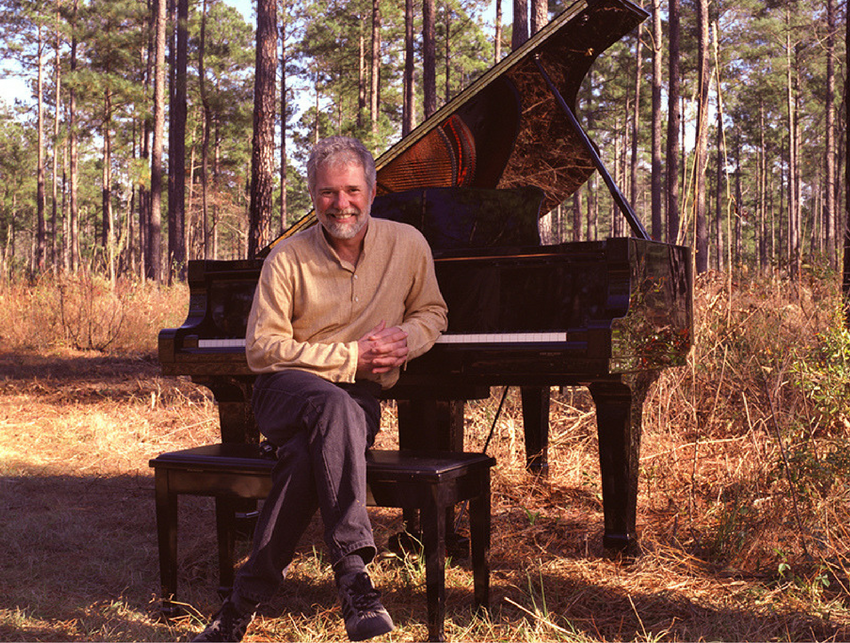 Image of Rolling Stones keyboardist Chuck Leavell sitting next to a piano in the woods