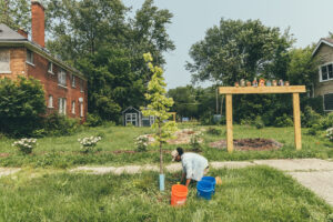Photo by Hans Isaacson for the National Association of State Foresters. Woman planting a tree near a community garden.